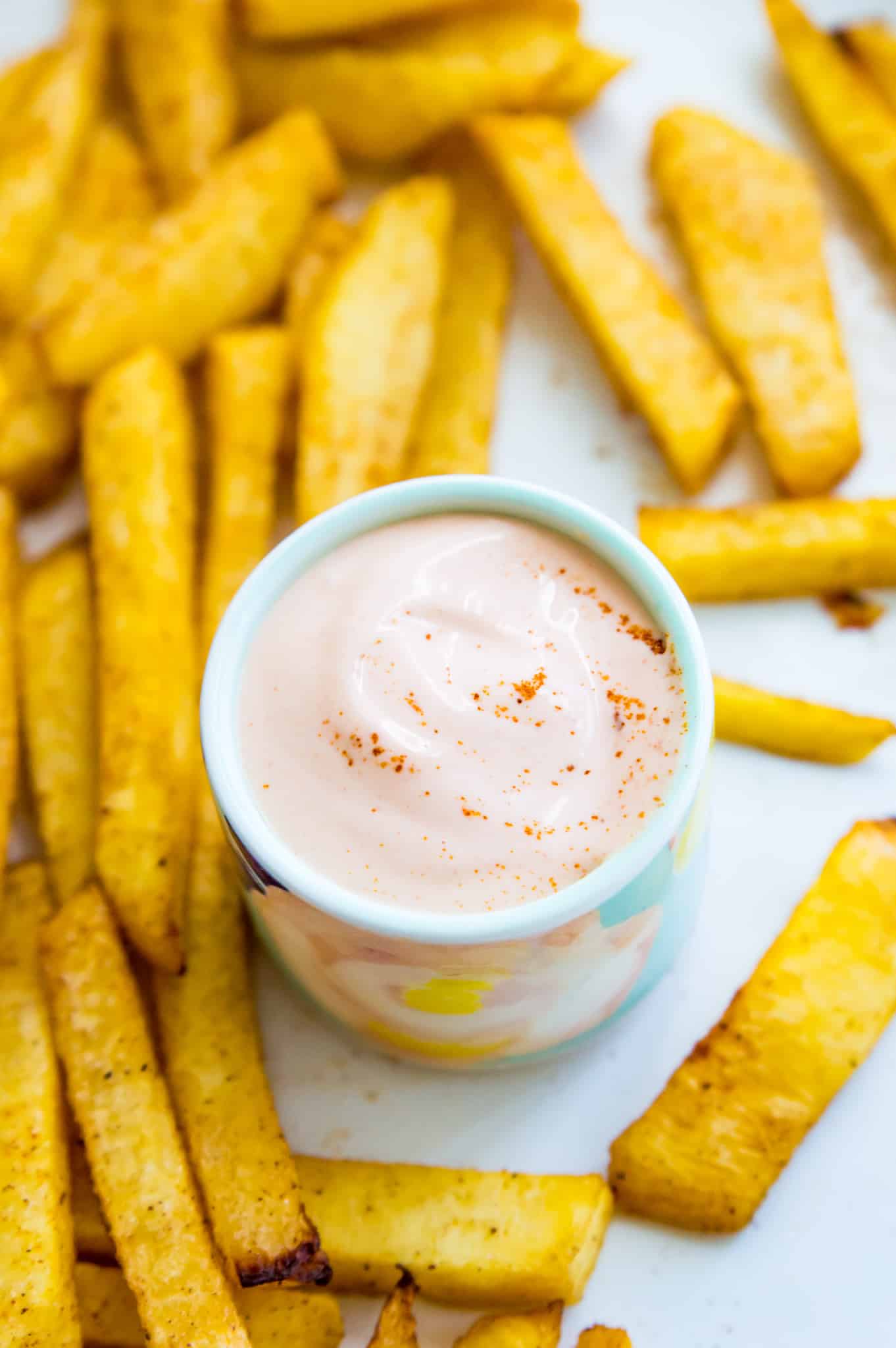 a small bowl filled with sriracha mayo surrounded by French fries