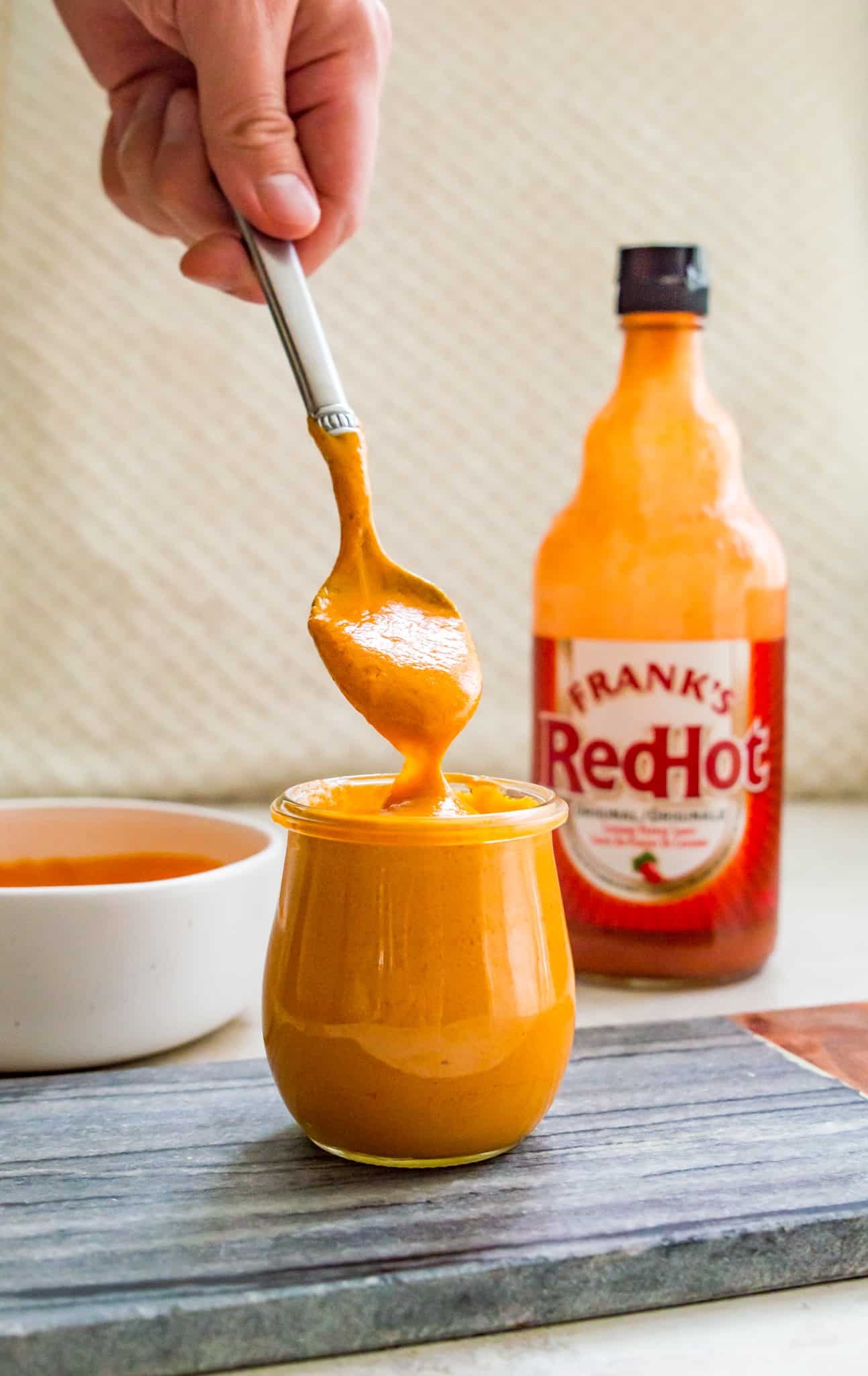 A jar of vegan buffalo sauce with a spoon coming out of it.