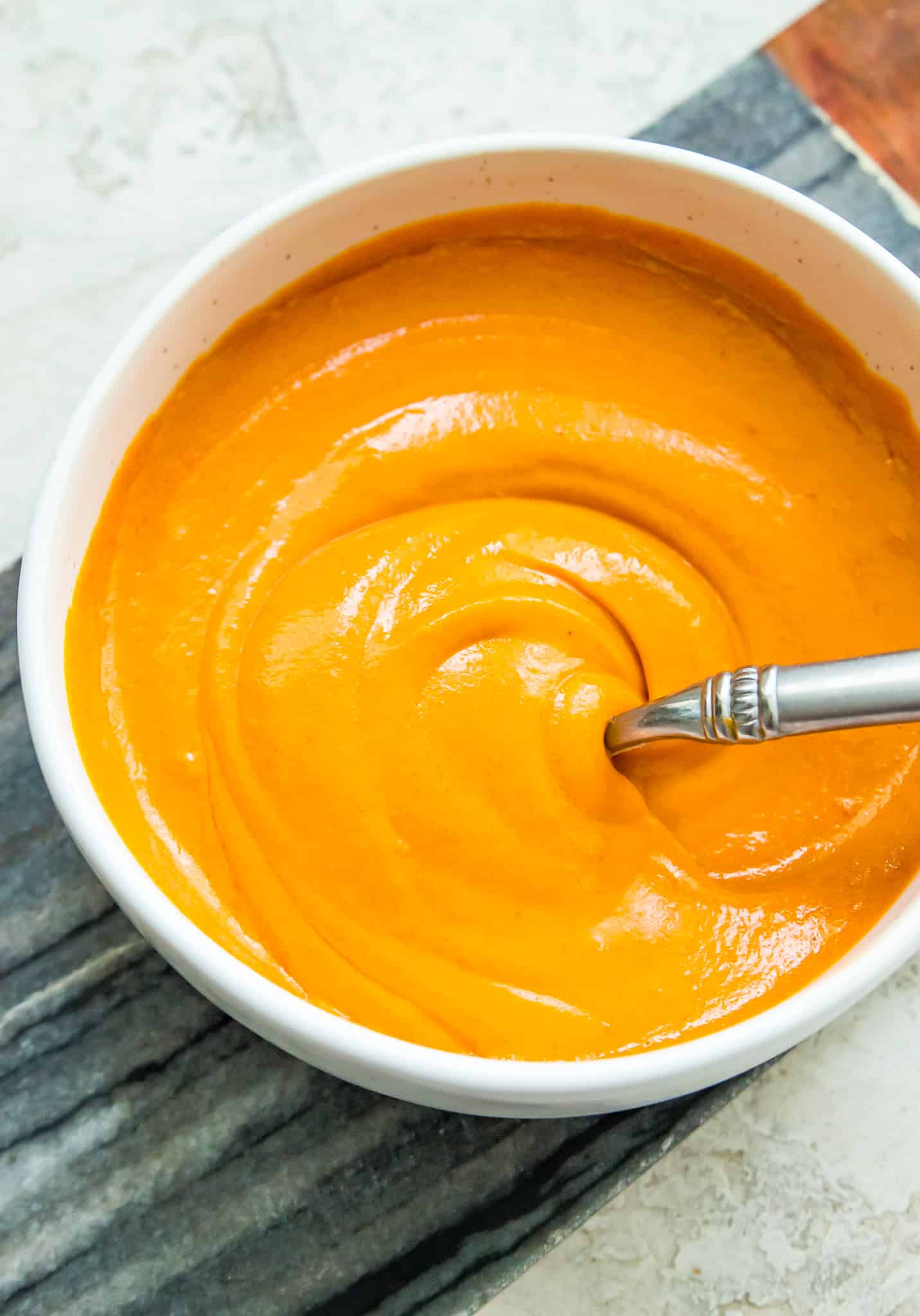 A bowl of vegan buffalo sauce with a spoon in it.