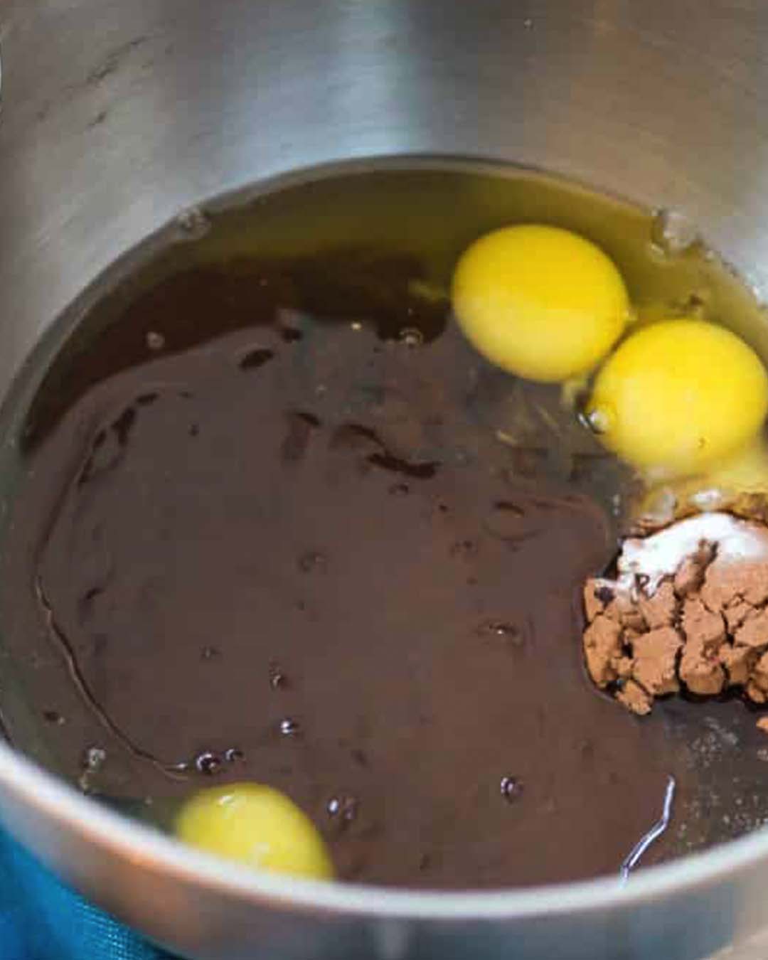 A metal bowl filled with eggs, cocoa powder and melted chocolate.