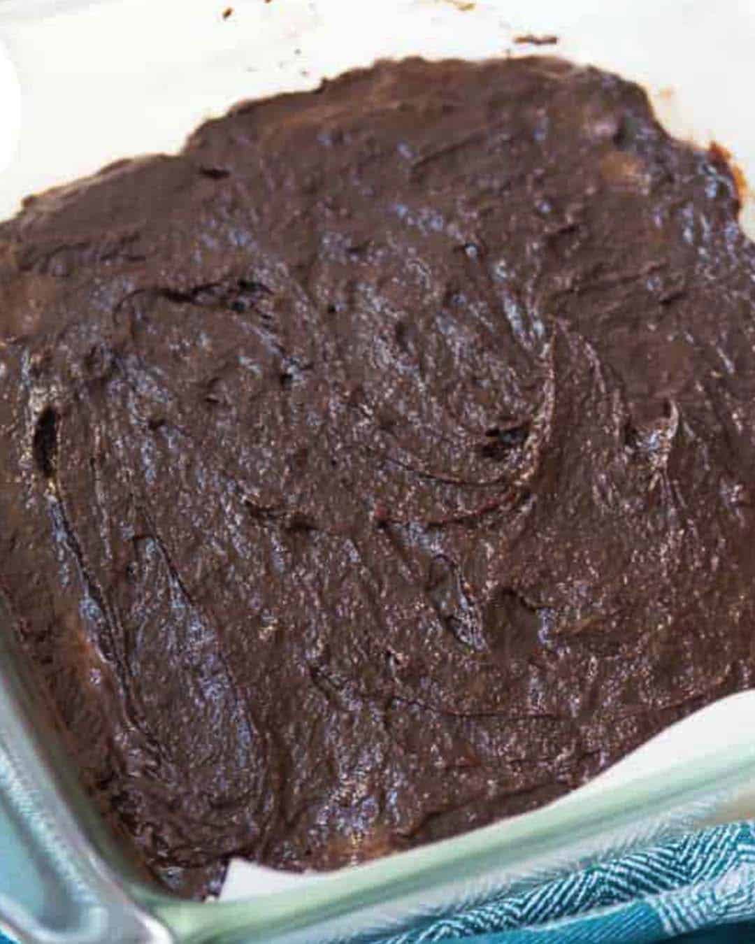 A baking dish lined with parchment paper with brownie batter in it.