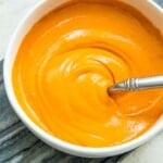 A bowl of vegan buffalo sauce with a spoon in it.