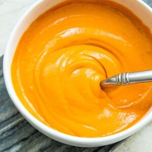 A bowl of vegan buffalo sauce with a spoon in it.