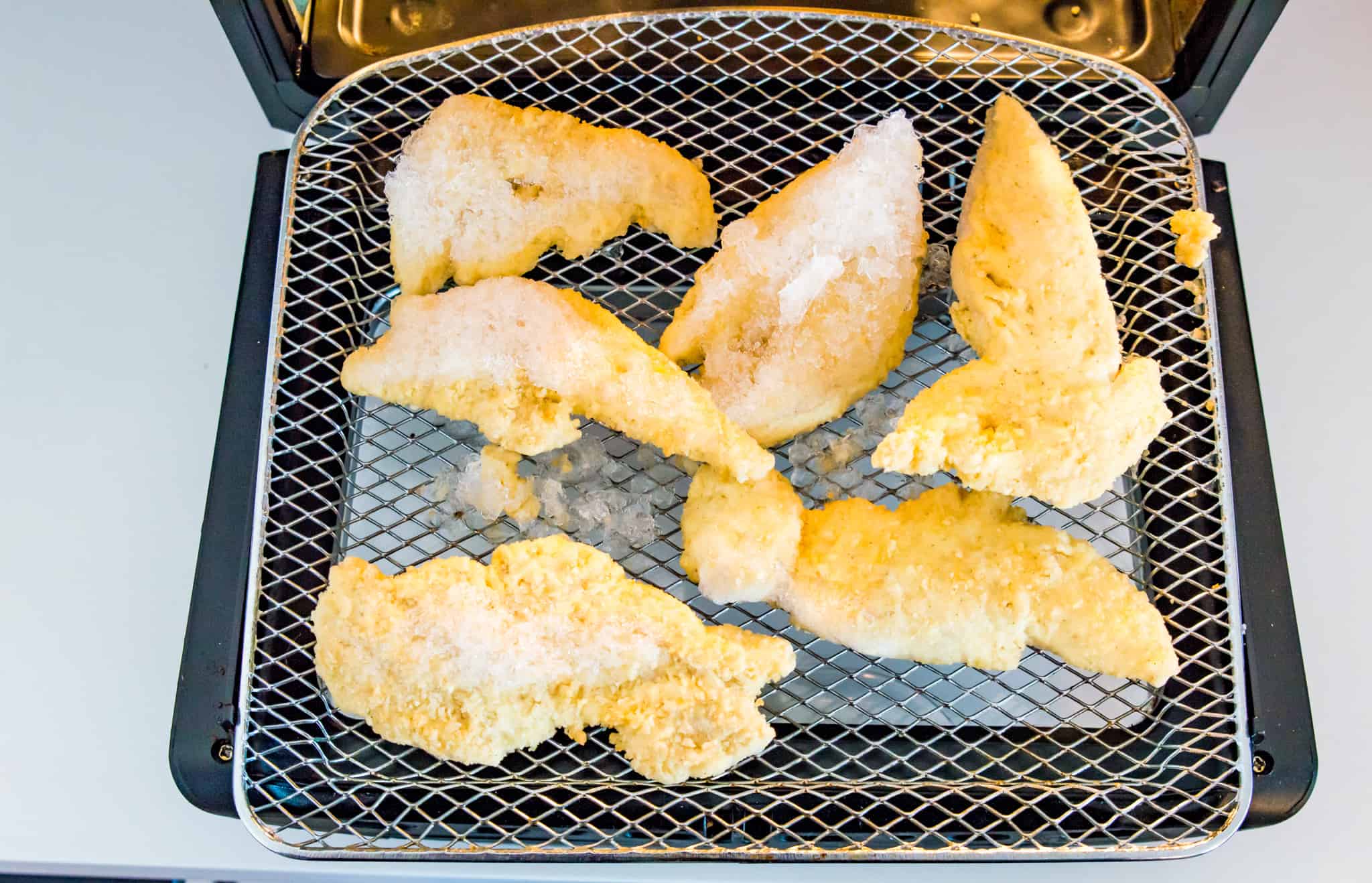 A air fryer tray with frozen chicken tenders on it