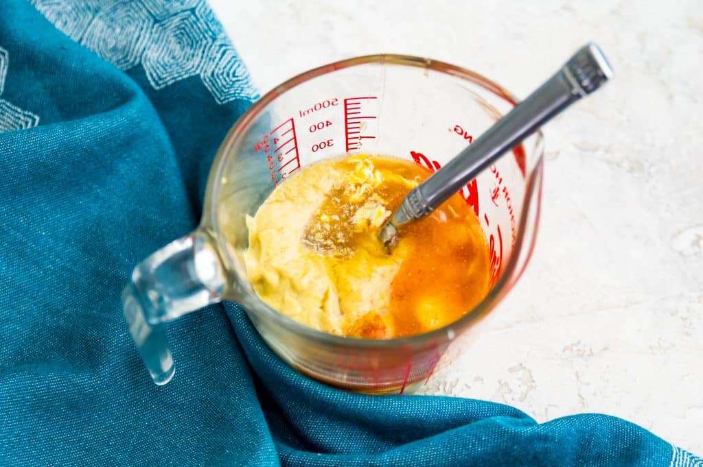 A glass measuring cup filled with mustard, mayonnaise, honey lemon juice and a spoon.