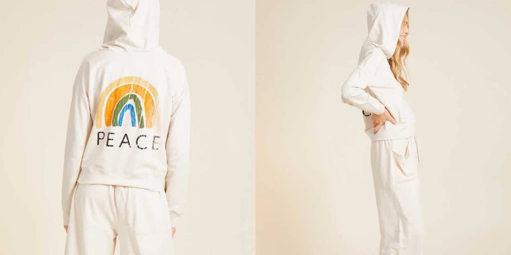 A girl wearing a YesAnd hoodie that is white with a rainbow and the word "peace" on the back.