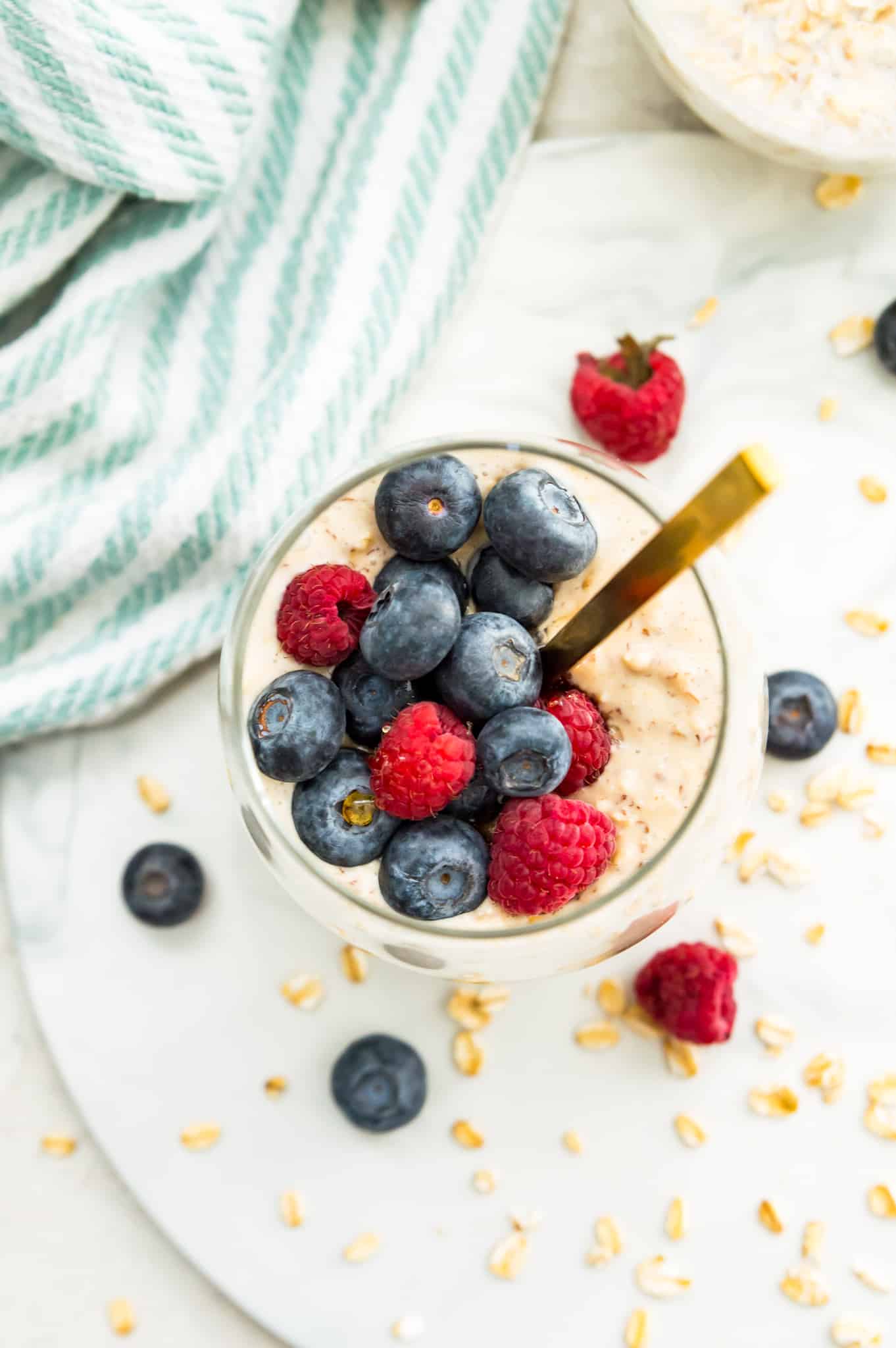 A jar of overnight oatmeal topped with blueberries and raspberries with a spoon in it.