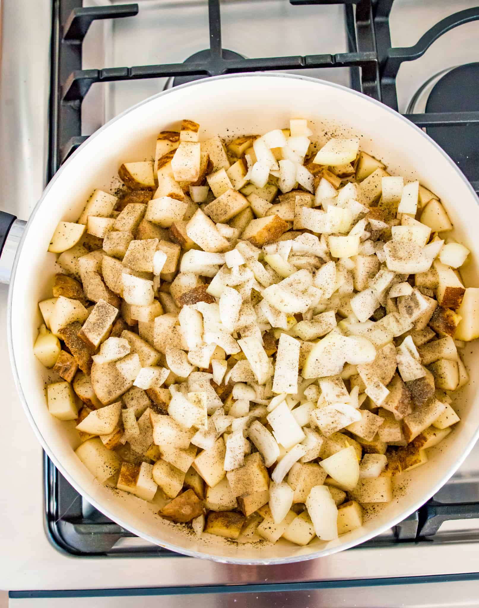 Chopped potatoes and onions being cooked in a skillet on the stovetop.