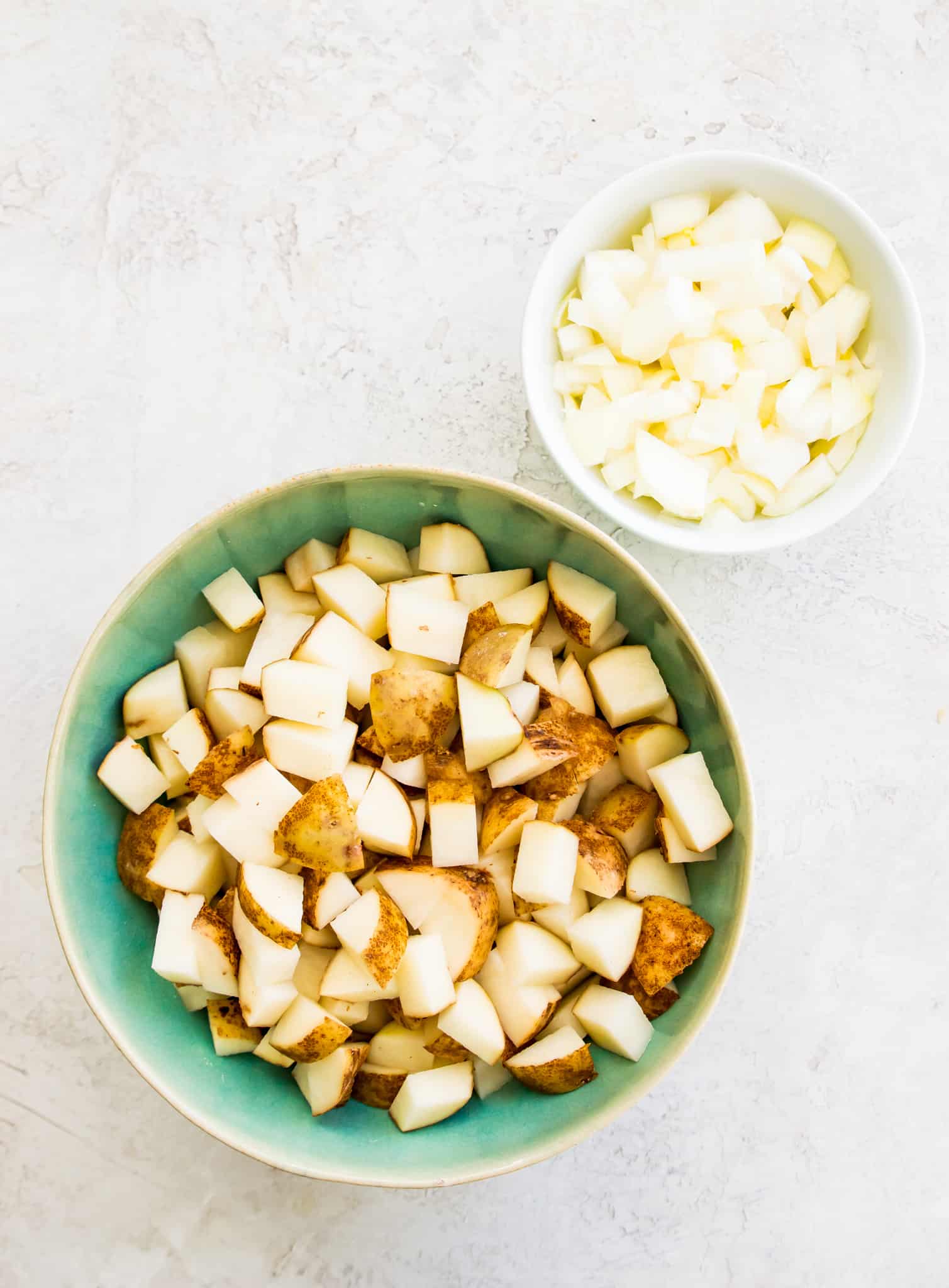 Bowls of chopped potatoes and chopped onions. 