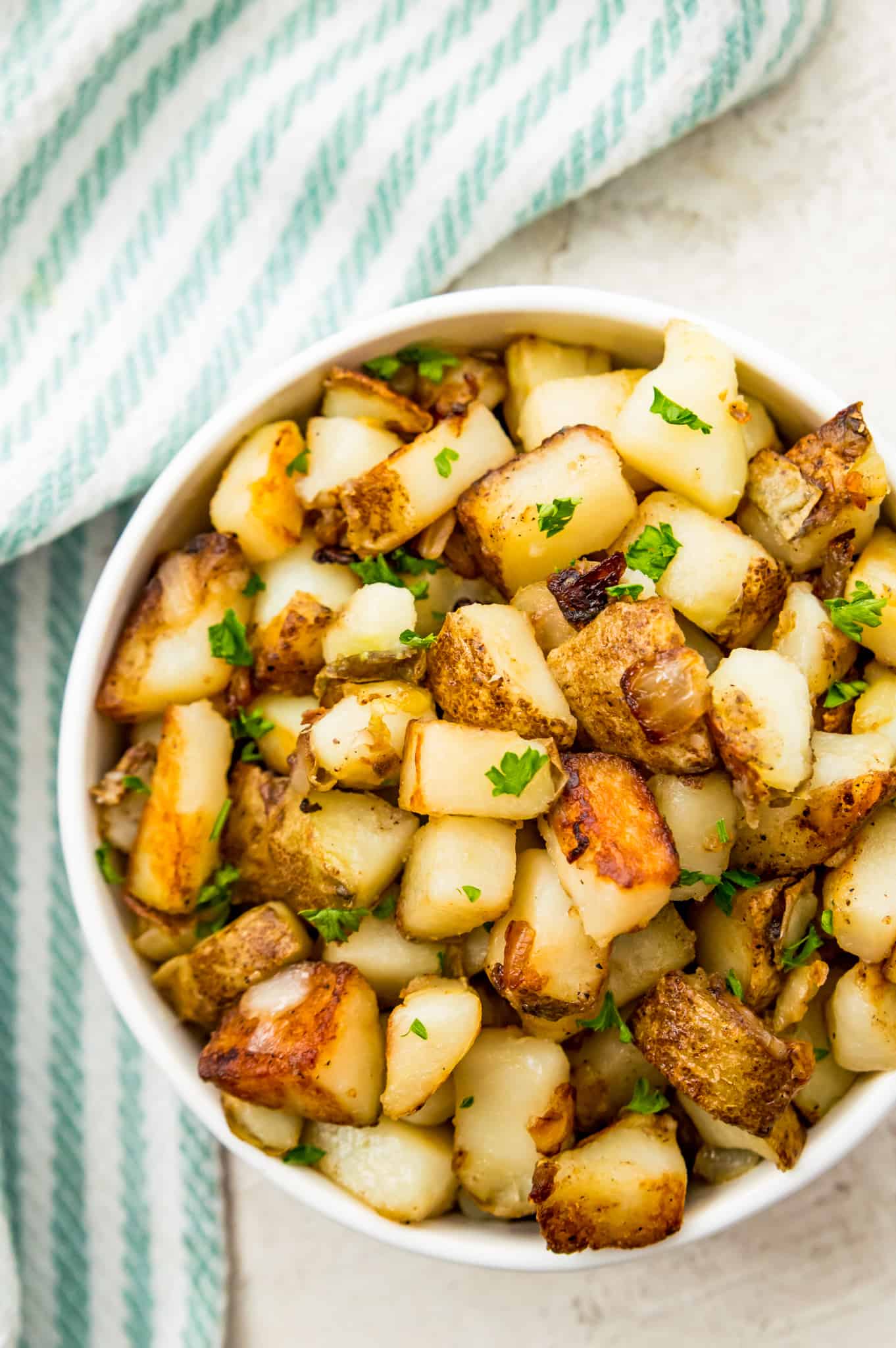 A bowl of southern fried potatoes garnished with fresh parsley. 
