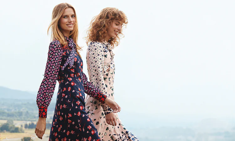 Two women in floral dresses by Boden walking in a field.