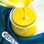 Honey mustard sauce being poured into a jar with a blue tea towel around it.