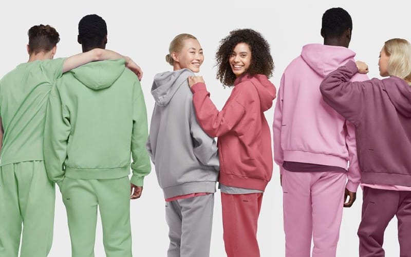 Six people in a row wearing different colours of sweatshirts and sweatpants including green, pink and purple. 