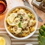 A bowl of spinach and artichoke casserole over noodles.