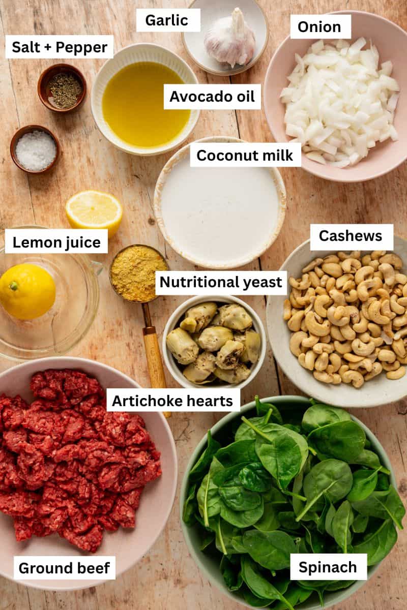 Different foods in bowls including chopped onion, cashews, spinach, ground beef, coconut milk and spices.