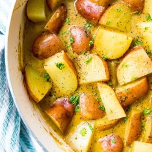 A pan filled with stewed potatoes topped with fresh herbs.