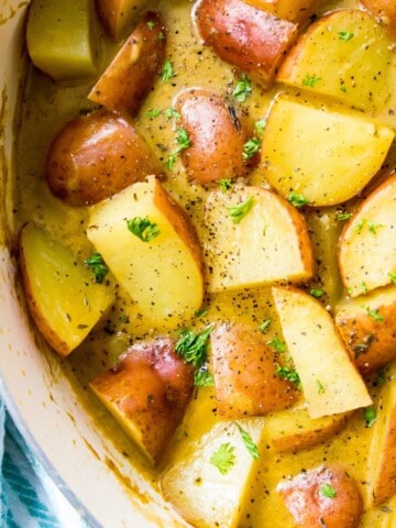A pan filled with stewed potatoes topped with fresh herbs.