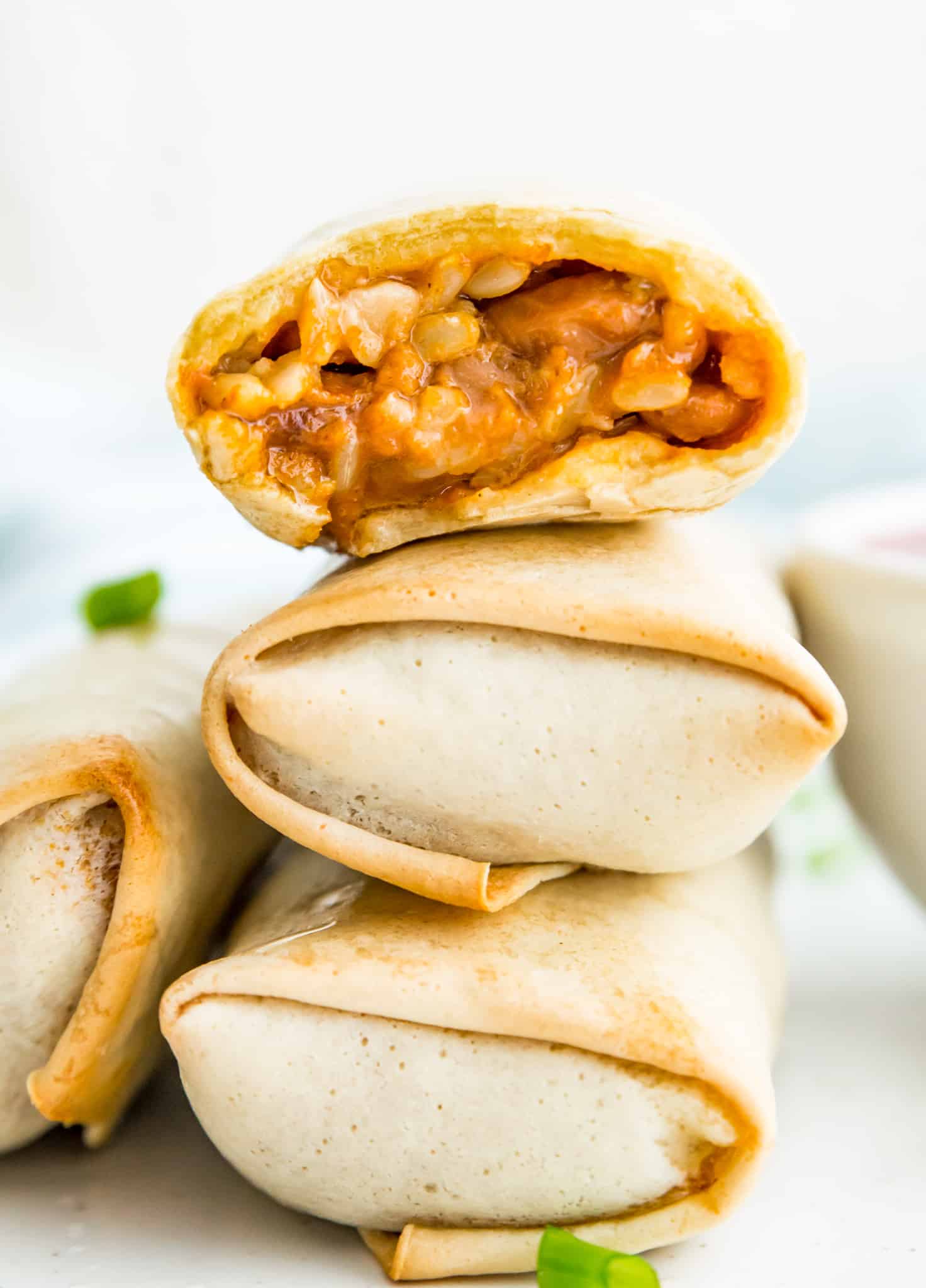 A stack of three cooked burritos, and the top one has a bite taken out of it.