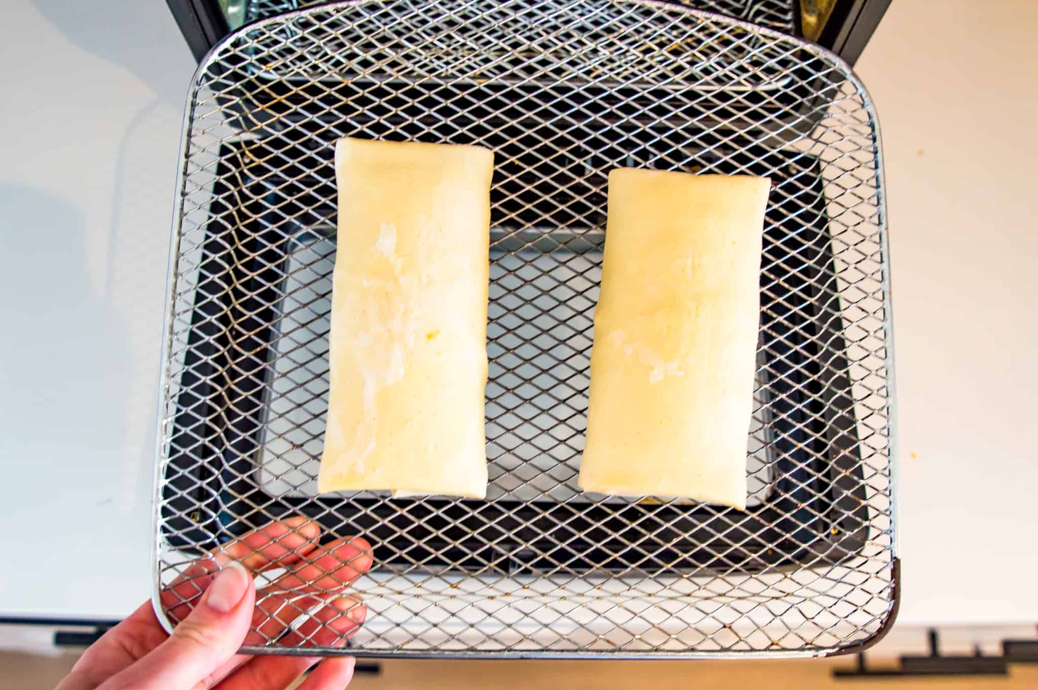 Two frozen burritos on an air fryer tray.