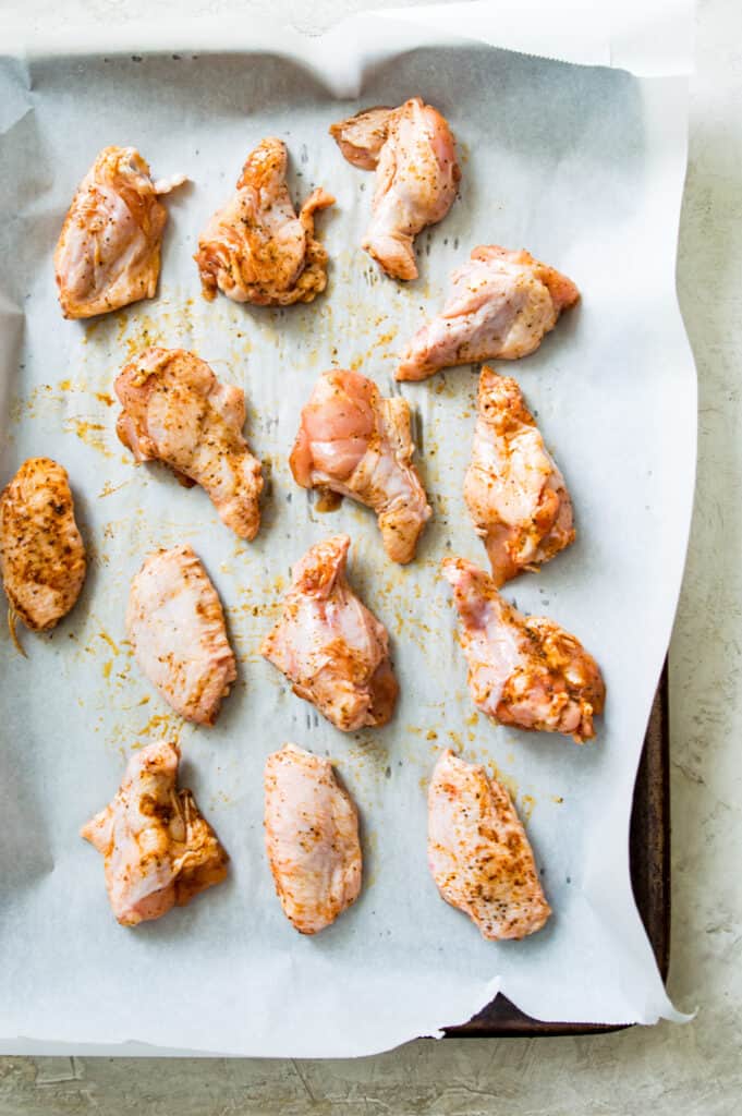 A baking sheet lined with parchment paper with chicken wings on it.