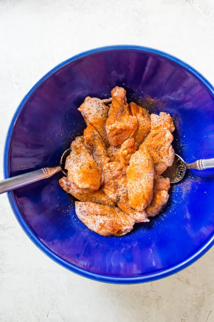 A large bowl filled with chicken wings and spices. 
