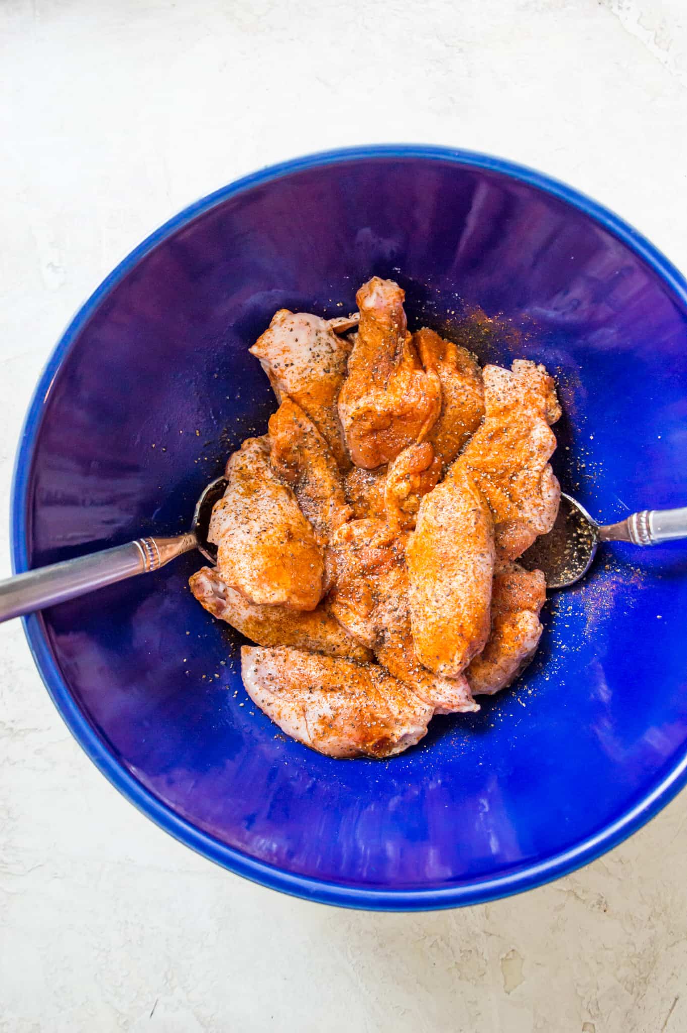 Raw chicken wings in a bowl coated in seasonings.