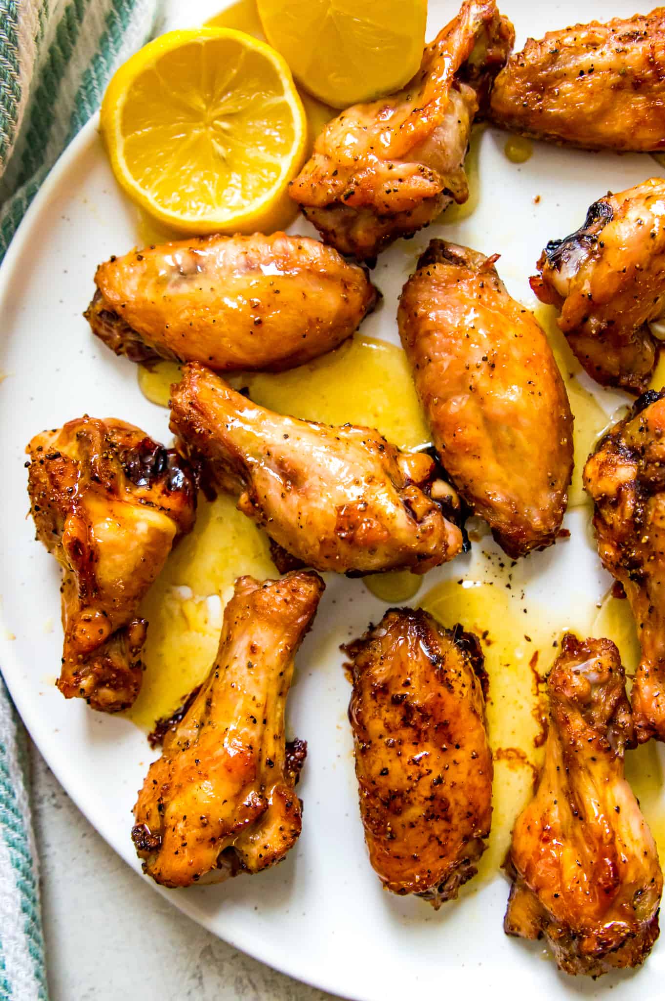 A plate of honey lemon pepper chicken wings with a lemon wedge on it.