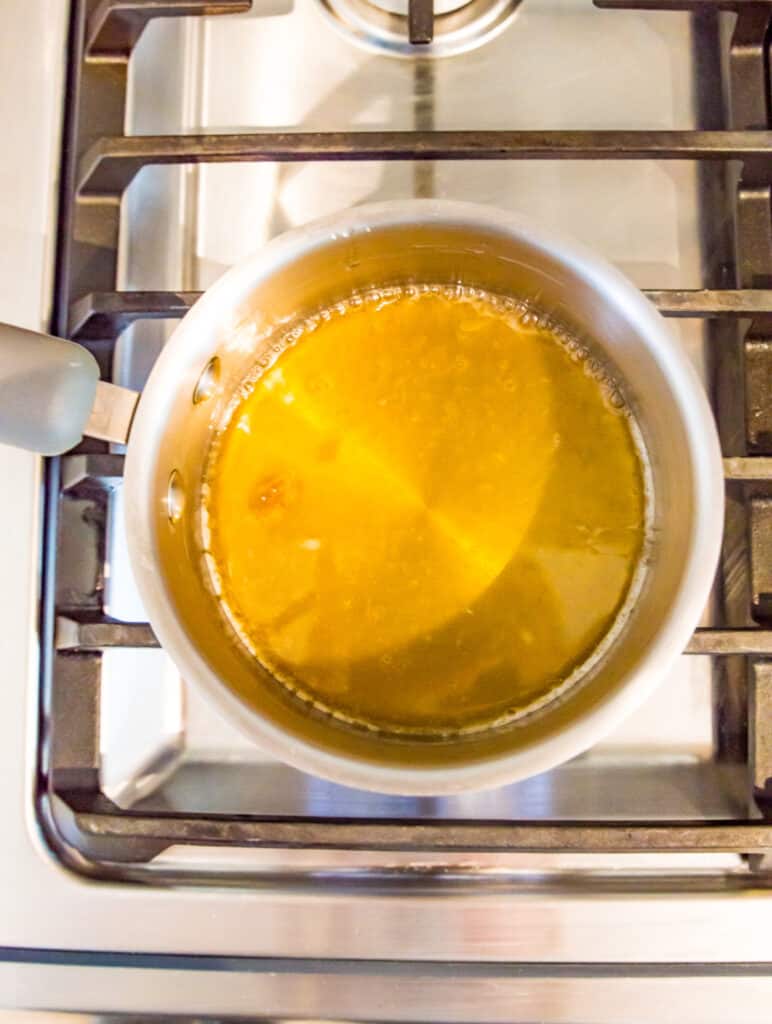A pot on the stovetop with a honey lemon pepper glaze boiling in it.