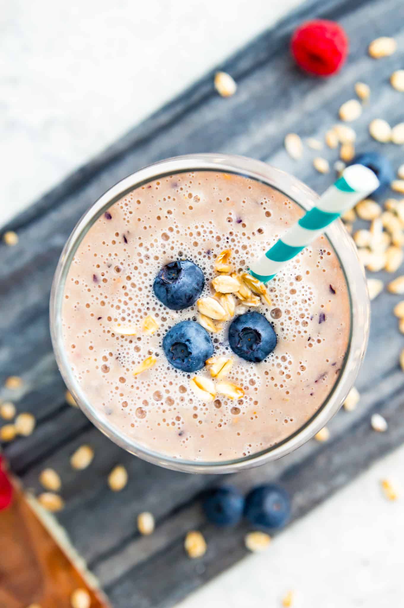 A glass full of an oat milk smoothie topped with fresh blueberries.
