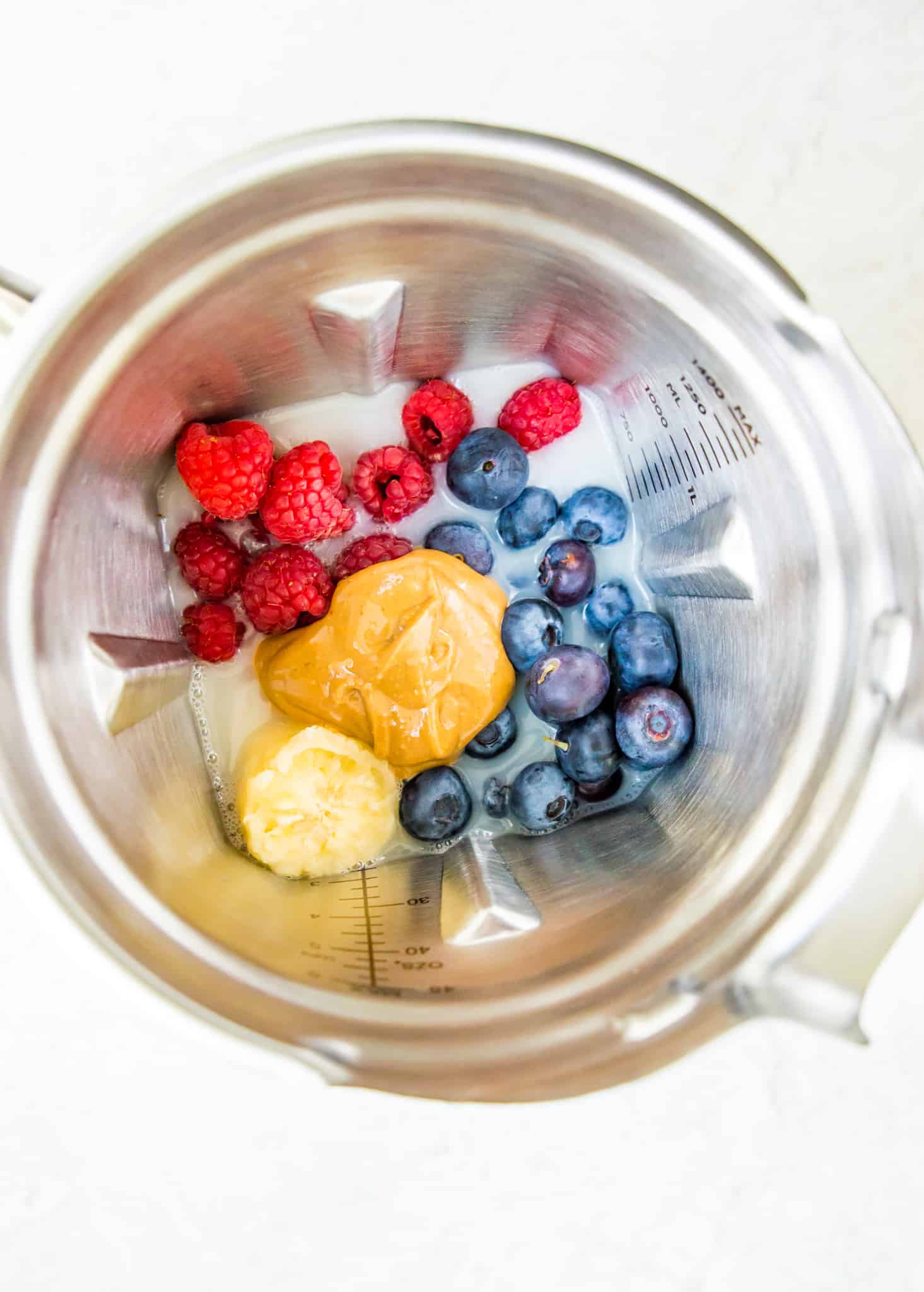 A blender with banana, blueberries, raspberries, peanut butter and oat milk in it.