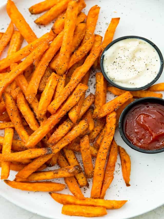 A plate of cooked sweet potato fries with sides of ketchup and mayonnaise. 