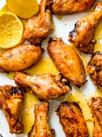 A plate of honey lemon pepper chicken wings with lemon wedges beside them.