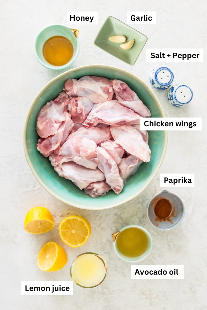 The ingredients needed for making honey lemon pepper wings in separate bowls including chicken wings, honey, garlic, oil and salt and pepper.