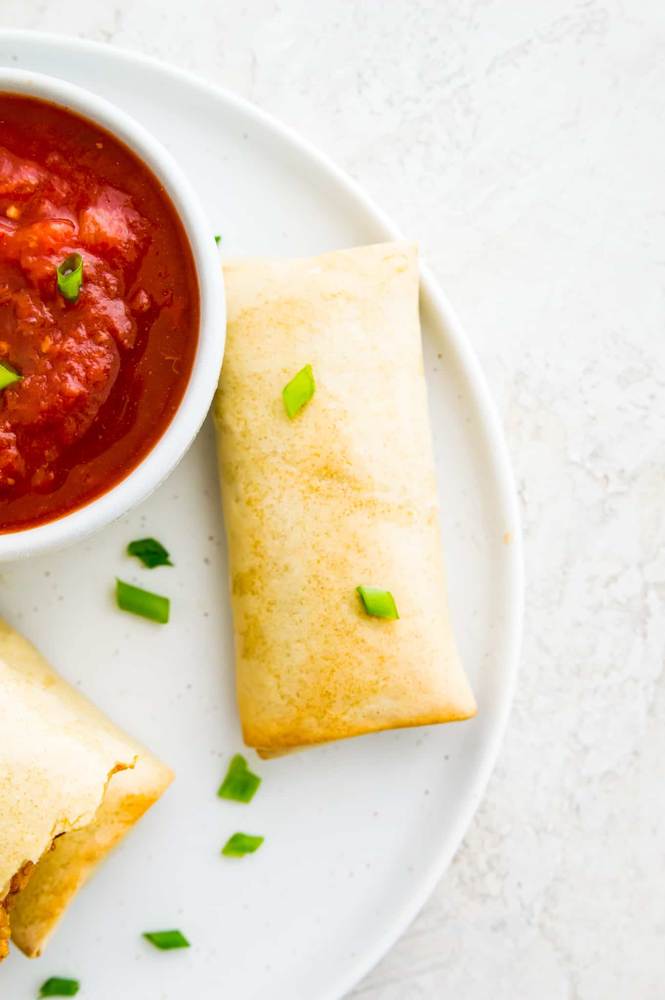 A cooked burrito on a plate garnished with green onion with a side of salsa beside it.