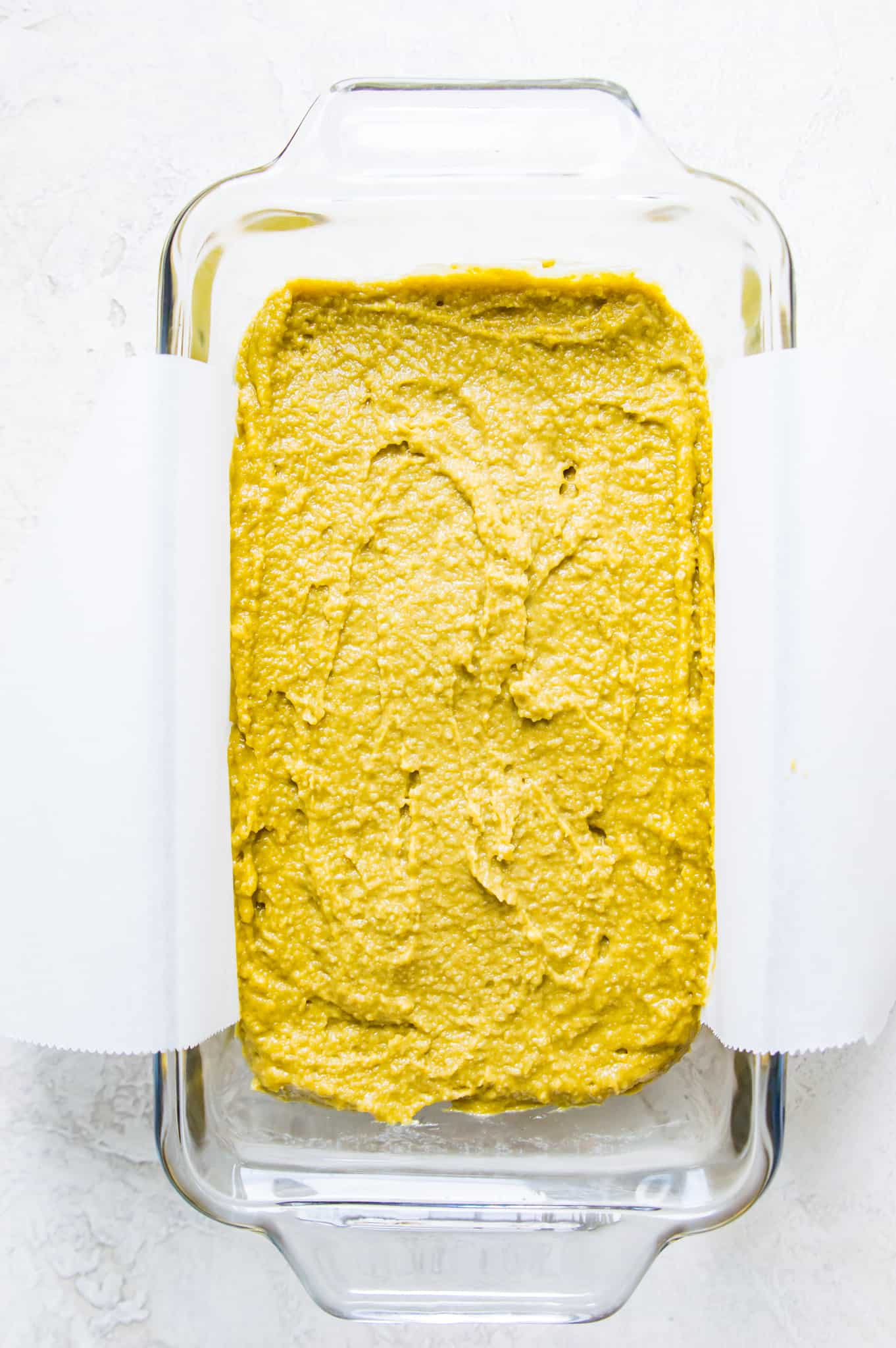 A glass bread pan lined with parchment paper with bread batter in it.