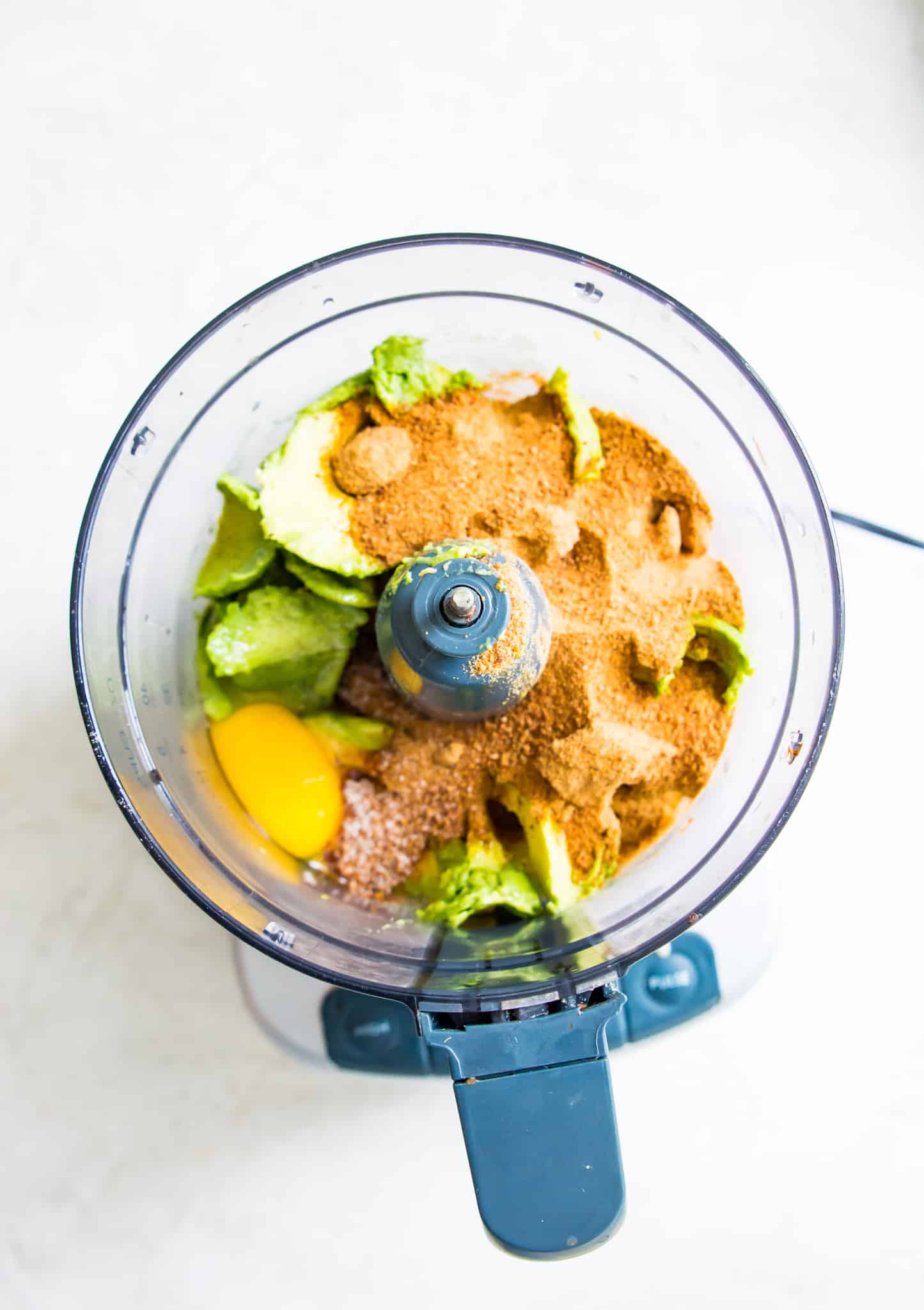 A food processor filled with sugar, eggs and avocado flesh.