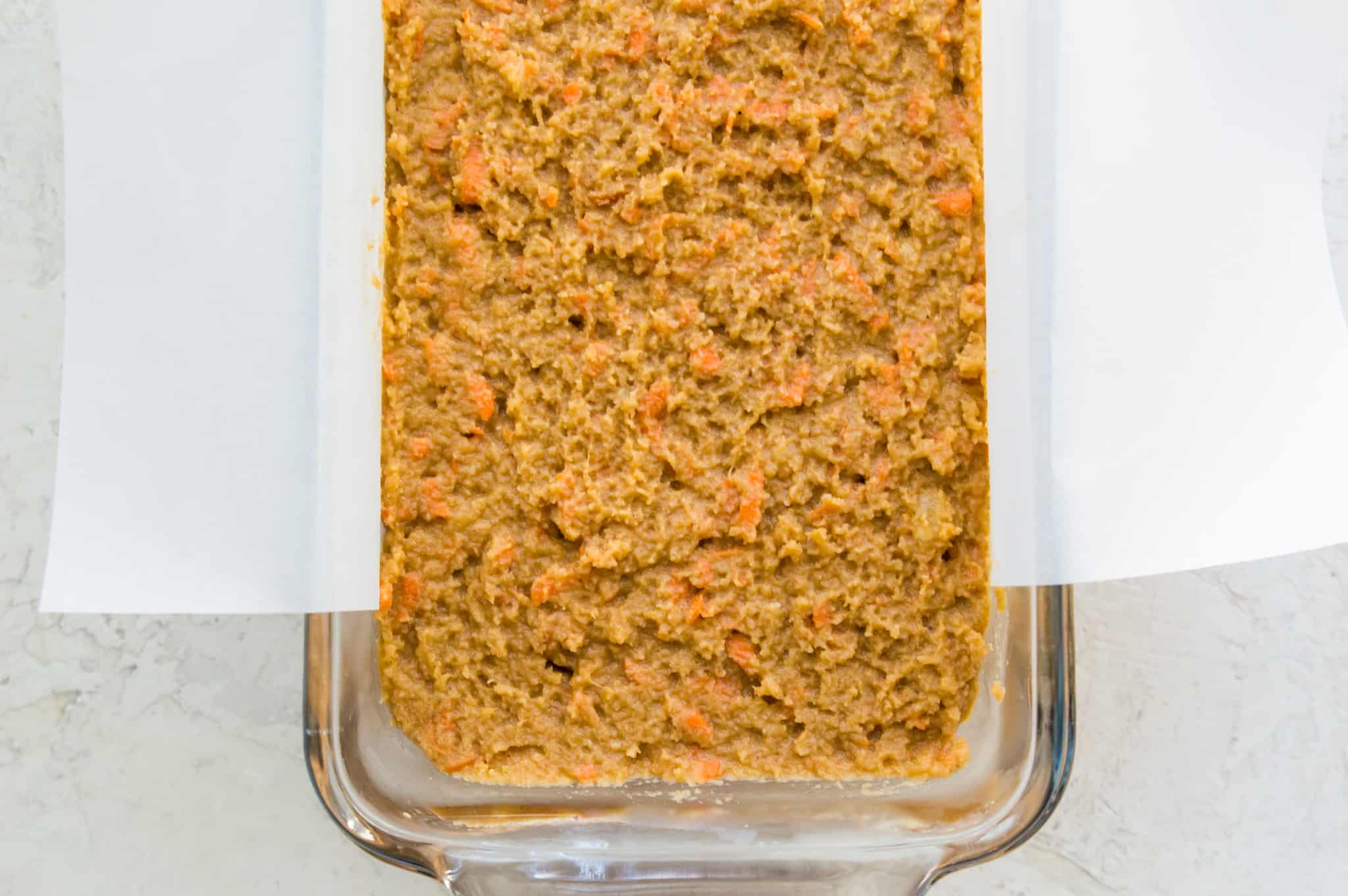 A bread pan lined with parchment paper with a carrot cake banana bread batter in it.