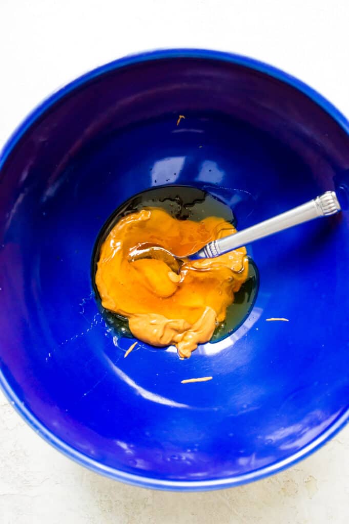 A bowl filled with honey and peanut butter with a spoon mixing the ingredients together.