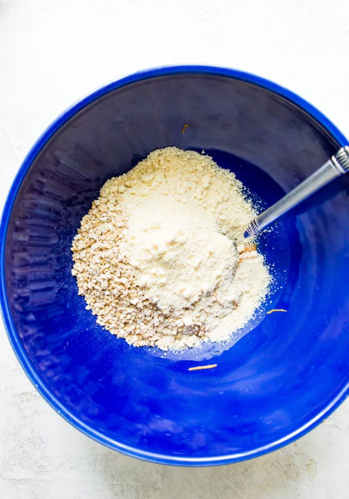 A bowl filled with oats and almond flour with a spoon in the ingredients.