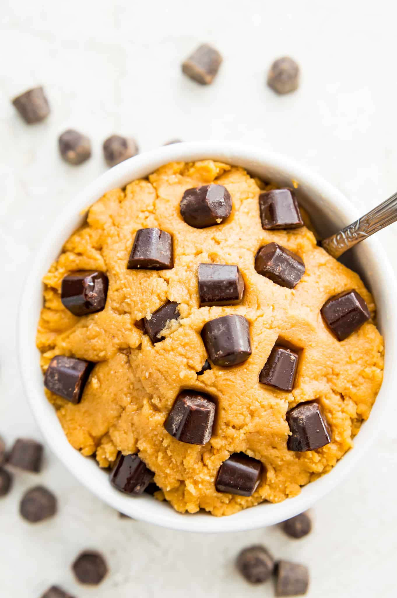 A bowl of raw cookie dough with chocolate chips on top and a spoon in it.