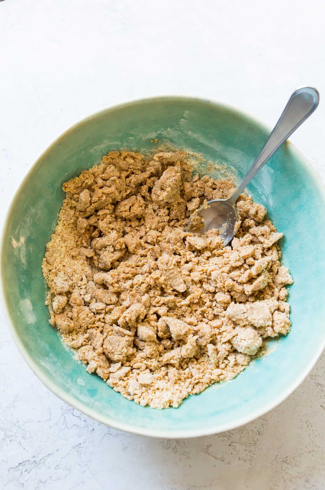 A bowl with the ingredients to make protein cookie dough in it with a spoon in it.