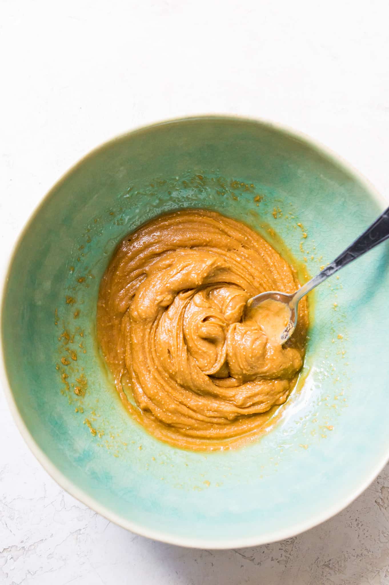 A bowl with peanut butter and syrup in it with a spoon. 