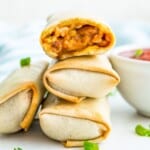 A stack of three cooked burritos and the top one has a bite out of it.