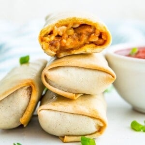 A stack of three cooked burritos and the top one has a bite out of it.