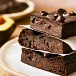 A stack of three avocado brownies topped with chocolate chips on a plate.