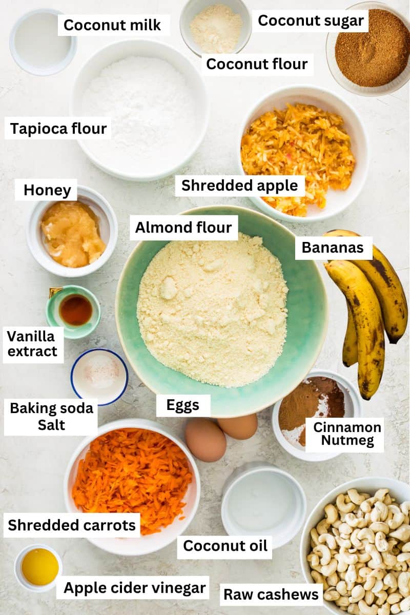 The ingredients for making carrot cake banana bread separated into bowls including flour, shredded carrots, eggs, honey, bananas, and sugar.