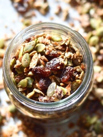 A jar full of grain free granola surrounded by granola pieces.