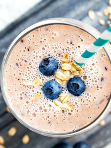 A smoothie in a glass topped with blueberries and oats with a straw in it.