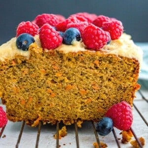 A loaf of paleo carrot cake banana bread topped with raspberries and blueberries.