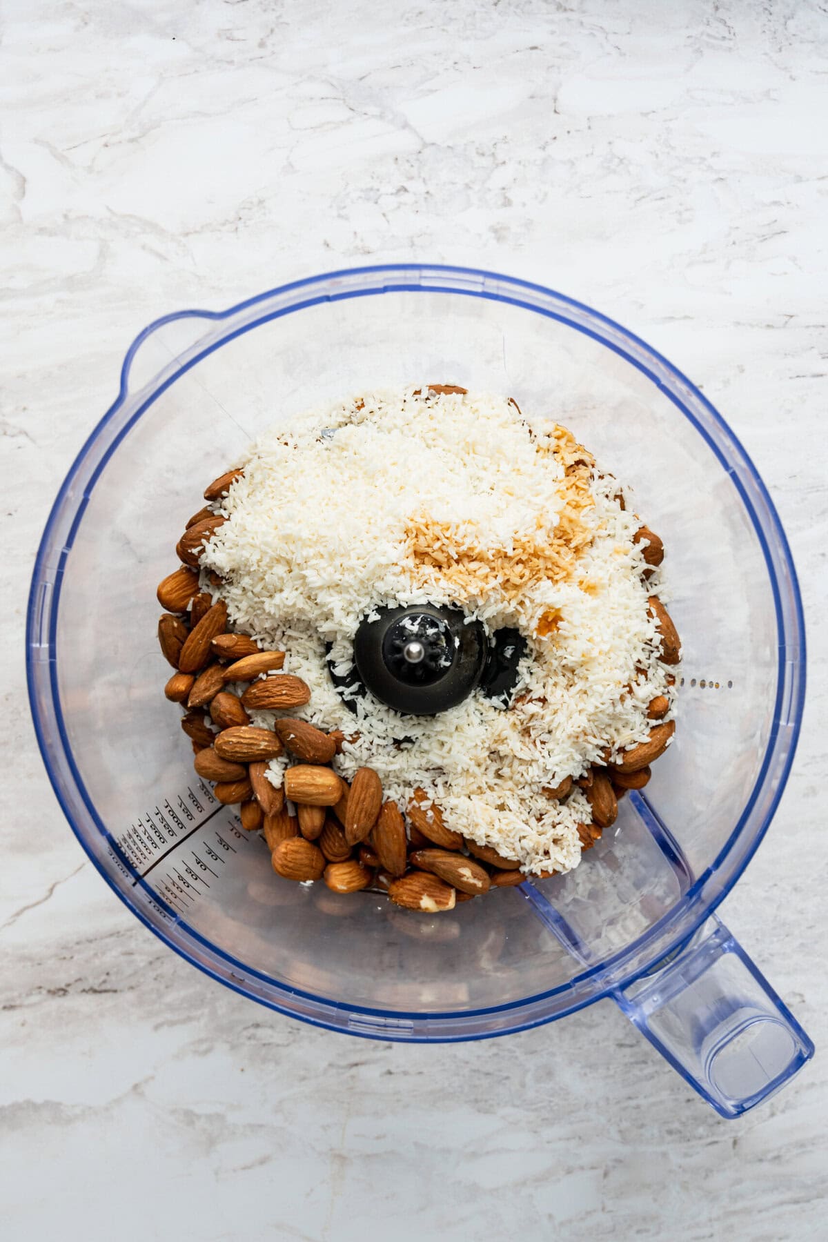 A food processor with almonds, shredded coconut and maple syrup in it.